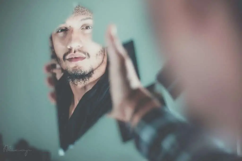 Man looking in a broken piece of a glass while holding it.